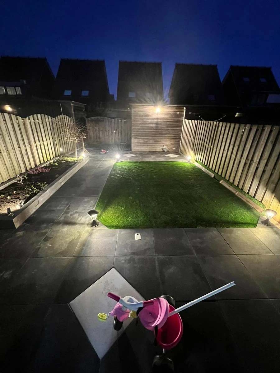 Verlichte achtertuin met strakke tuinbestrating, verhoogde border met planten en gras